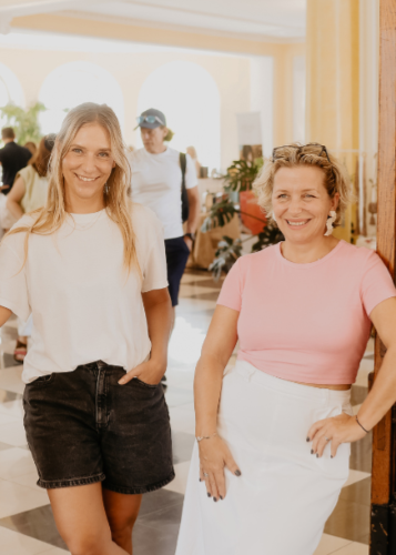 Két mosolygó nő áll egy rendezvényen vagy folyosón. Barátok, kollégák, esemény, mosoly, nyár, társaság.