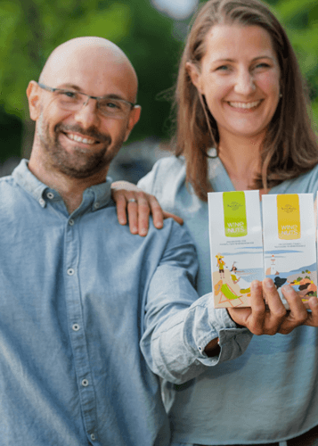 Egy mosolygós pár áll szabadban, a nő két fehér dobozt tart a kezében, melyeken a "WINE NUTS" felirat látható. A férfi balra, kissé elmosódva, bajusszal és szemüveggel néz a kamerába, kék inget visel. A nő jobbra, szintén mosolyog, haja kibontva. A háttér